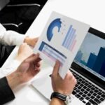 A group of people analyzing graphs displayed on a laptop screen, engaged in discussion and collaboration.